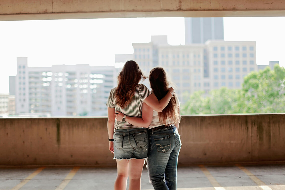 Dos personas abrazadas mirando hacia la ciudad desde un espacio elevado — símbolo de cuidado, pertenencia y deseo de una ciudad más habitable y acogedora